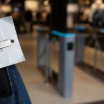 RFID Scorecard A close-up of an RFID anti-theft tag with a barcode on clothing. In the background, out-of-focus security gates stand at a store's exit, demonstrating technology used for inventory management and loss prevention in modern retail environments to combat shoplifting.