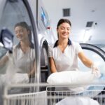 Essential Healthcare CoreRFID Dry cleaning service female worker loading industrial washing machine with clothes and linen.