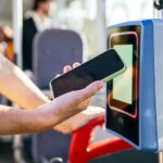 NFC Forum Woman using mobile payment on a contactless reader inside a public city bus, representing modern travel and technology